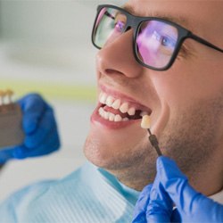 Man smiling as dentist holds shade guide to his teeth