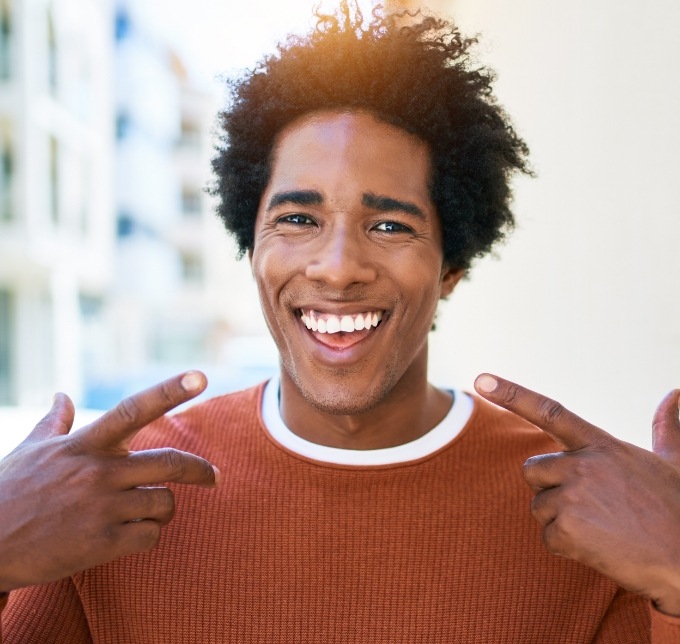 Man in orange shirt pointing to his smile