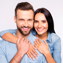 A man and woman wearing denim shirts and hugging after receiving cosmetic dentistry treatments to improve their smiles