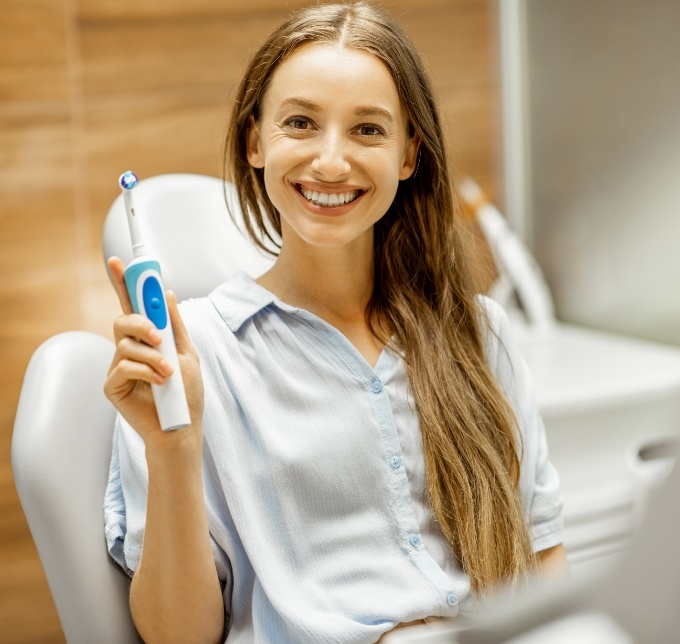 Woman holding an electric toothbrush in a dental chair