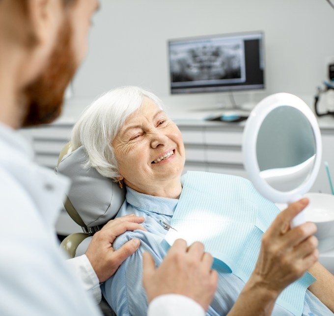 Senior woman sitting in a dental chair looking at smile in mirror