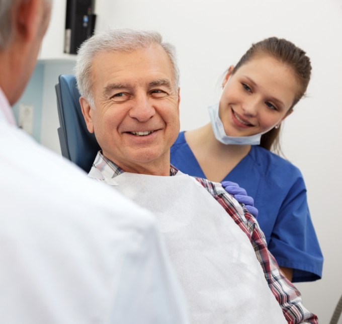 Senior man in dental chair looking at dental team members