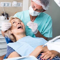 An older woman has her teeth checked by a dentist to determine if she needs full-mouth reconstruction