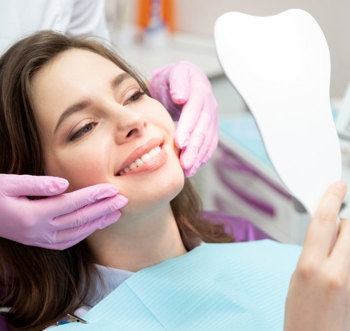 Female dental patient checking smile in mirror after treatment