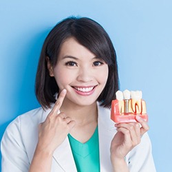 Woman pointing to her smile while holding model of dental implant