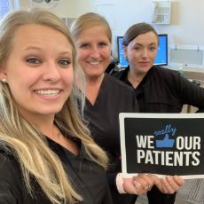 Three dental team members holding We Thumbs Up Our Patients sign