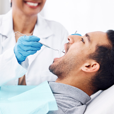 Dentist checking a male patient’s mouth during follow-up exam