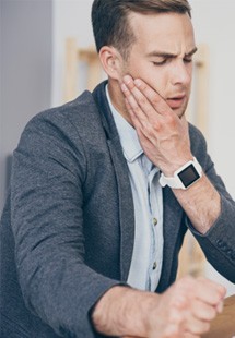 Wincing man holding his cheek in pain