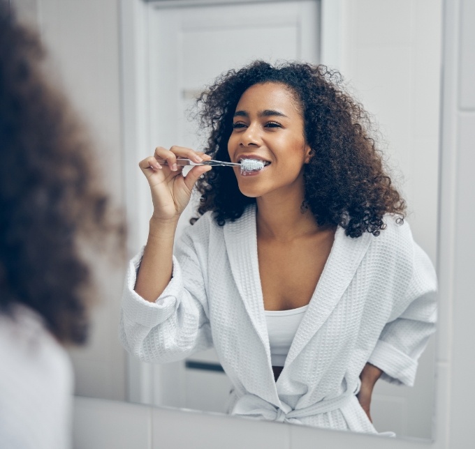 Woman brushing her teeth in the bathroom mirror