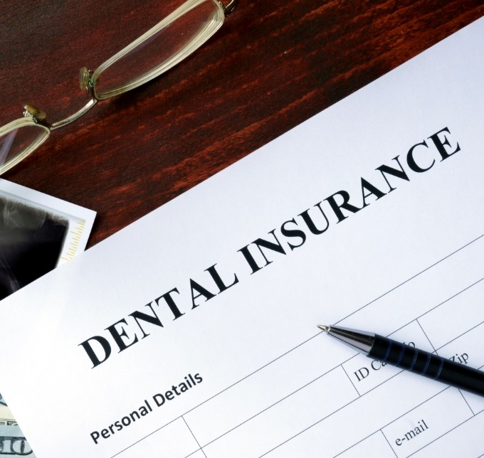 Dental insurance form on desk with pen and glasses