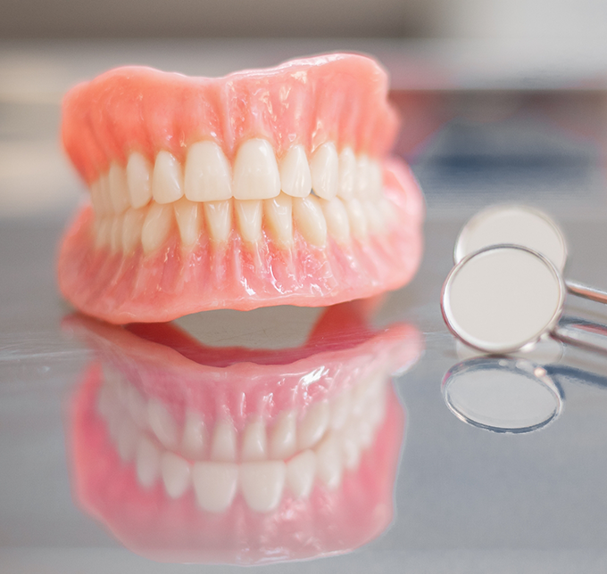 Set of full dentures on a tray next to a dental mirror