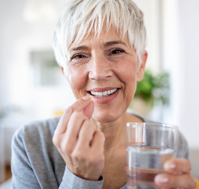 Senior woman holding a pill and a glass of water
