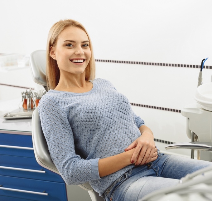 Blonde woman in blue sweater sitting in dental chair and smiling