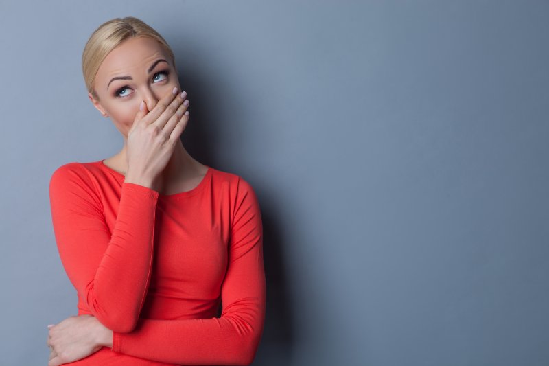 a woman wearing a red blouse and covering her mouth because of her gummy smile