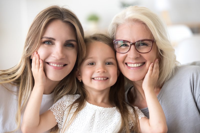 three generations of women with the grandmother smiling after undergoing full-mouth reconstruction