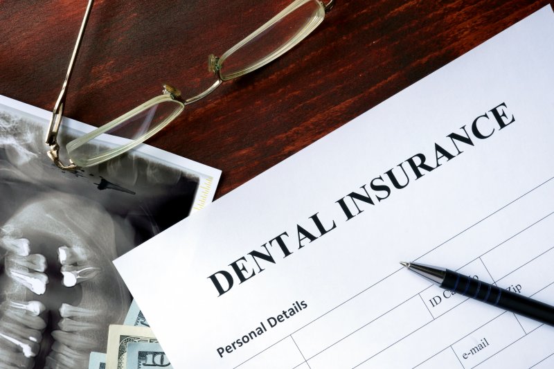 a table complete with a dental X-ray, glasses, a dental insurance form, and a pen